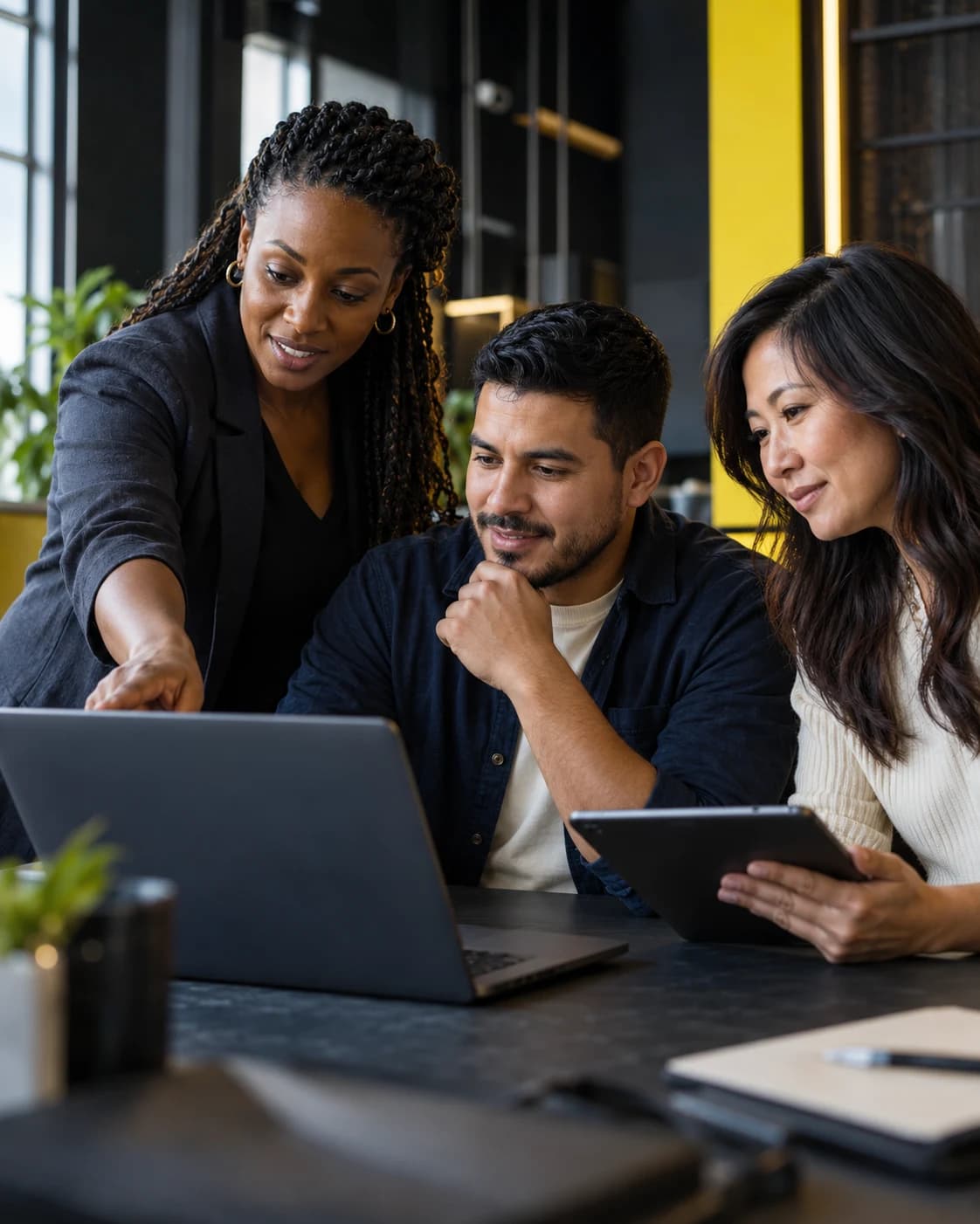 A team collaborating around a laptop and tablet in a modern training studio with yellow accents.